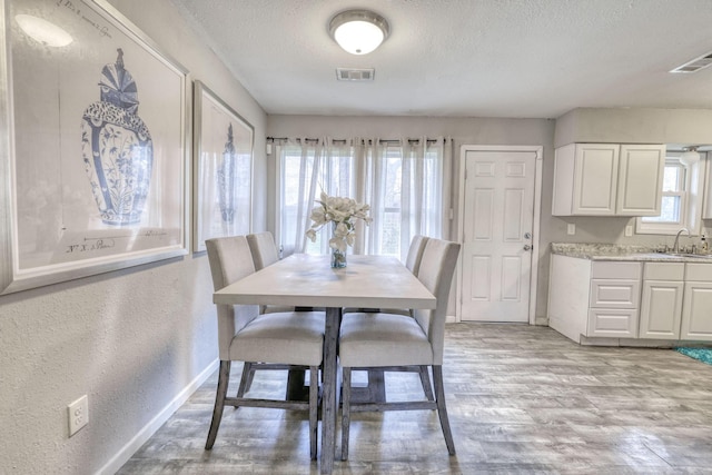 dining area featuring sink, light hardwood / wood-style flooring, and a textured ceiling