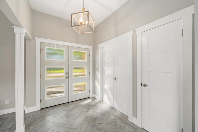 entrance foyer with ornate columns, parquet floors, an inviting chandelier, and french doors