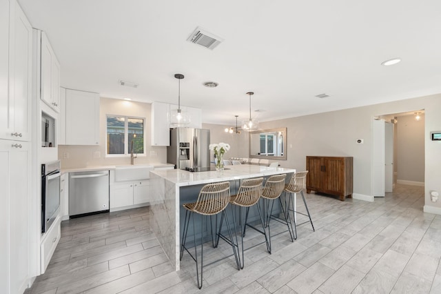 kitchen with sink, white cabinetry, a kitchen island, pendant lighting, and stainless steel appliances