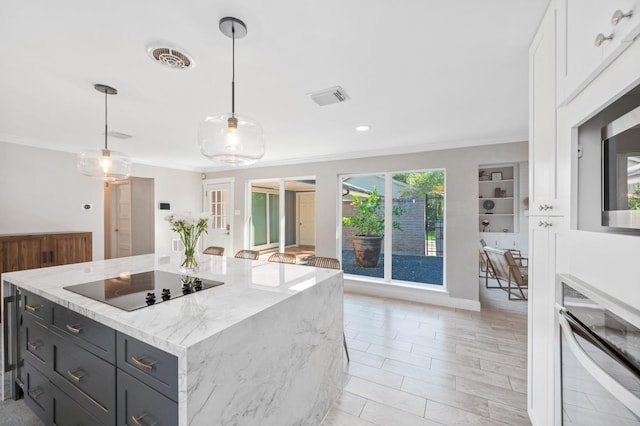 kitchen with hanging light fixtures, a center island, crown molding, light stone countertops, and black electric cooktop