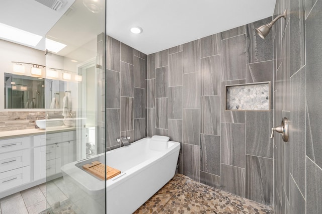 bathroom with tile walls, backsplash, a bathtub, a skylight, and vanity