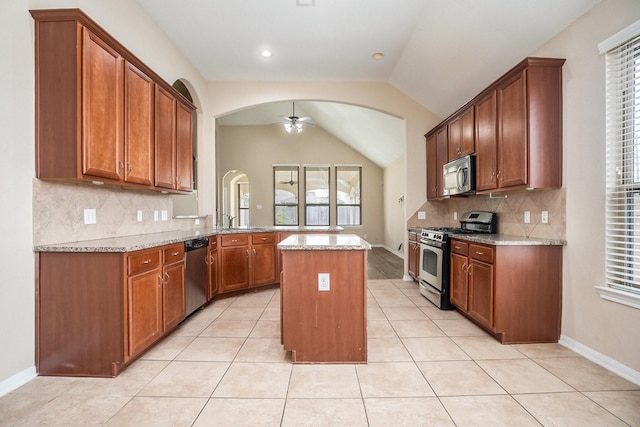 kitchen featuring ceiling fan, stainless steel appliances, light stone countertops, and a kitchen island