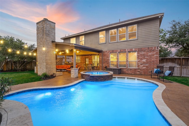 pool at dusk with a yard, a fenced backyard, a pool with connected hot tub, and a patio