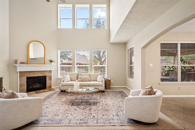 tiled living room with a high ceiling, baseboards, plenty of natural light, and a tiled fireplace