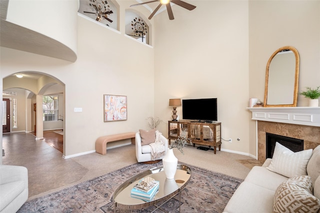 living area with baseboards, a high ceiling, arched walkways, and a tile fireplace