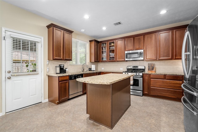 kitchen with visible vents, a kitchen island, light stone countertops, stainless steel appliances, and a sink