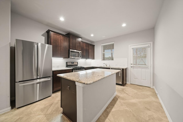 kitchen with a kitchen island, sink, dark brown cabinetry, stainless steel appliances, and light stone countertops