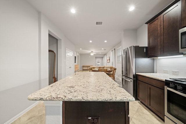 kitchen featuring light stone counters, a center island, dark brown cabinets, appliances with stainless steel finishes, and backsplash