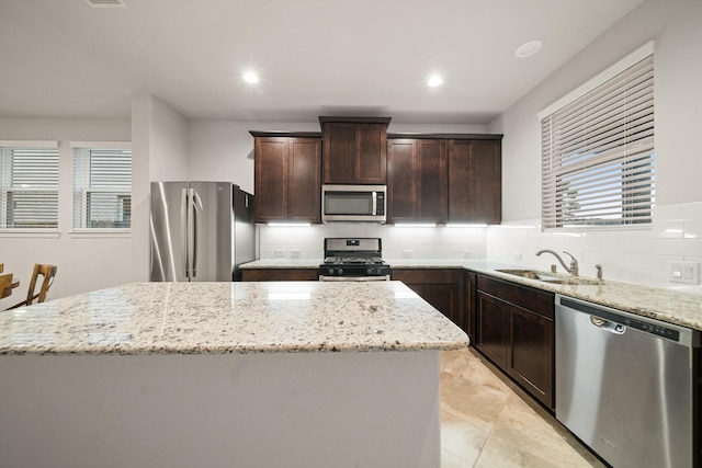 kitchen with a kitchen island, light stone countertops, appliances with stainless steel finishes, and sink