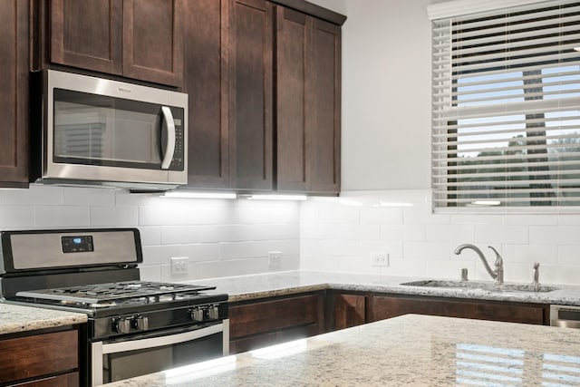 kitchen featuring tasteful backsplash, light stone countertops, appliances with stainless steel finishes, and sink