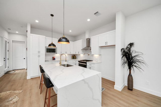 kitchen featuring decorative light fixtures, sink, a kitchen island with sink, stainless steel appliances, and wall chimney exhaust hood