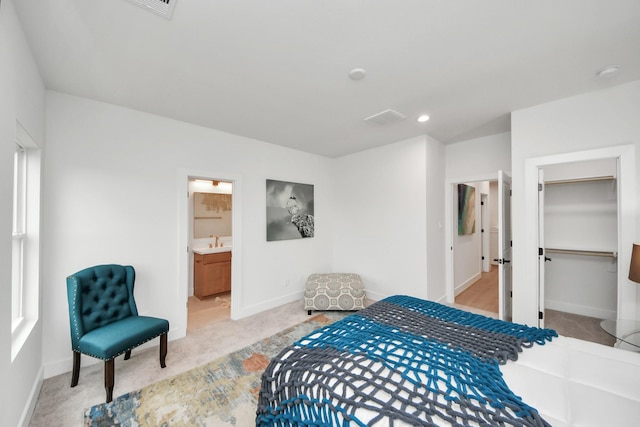 bedroom with light colored carpet, ensuite bathroom, sink, and a walk in closet