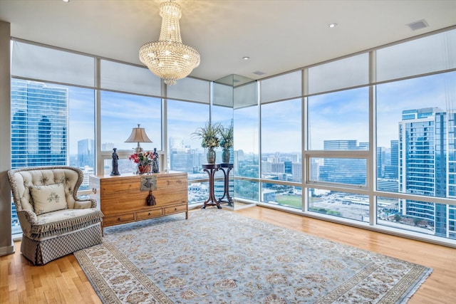 sitting room with visible vents, a notable chandelier, a city view, wood finished floors, and a wall of windows