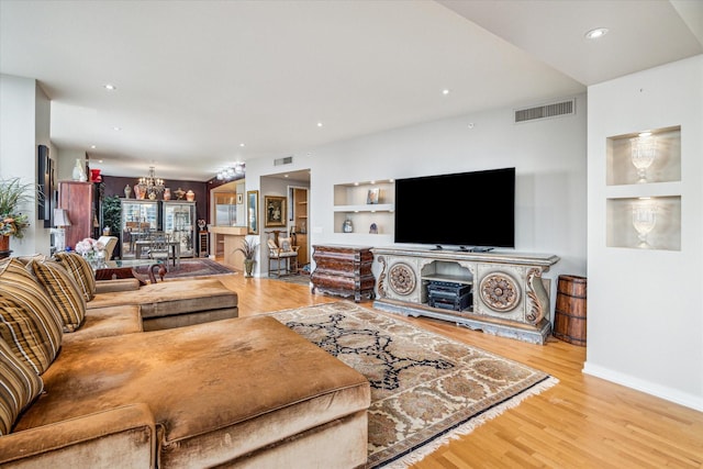 living room with a notable chandelier, built in features, and light hardwood / wood-style floors