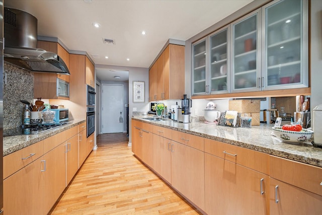 kitchen with sink, gas cooktop, light stone countertops, wall chimney exhaust hood, and light wood-type flooring