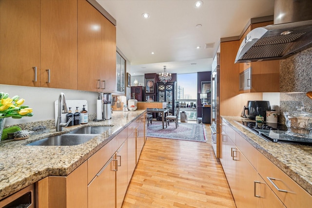 kitchen with wall chimney exhaust hood, sink, light hardwood / wood-style flooring, gas cooktop, and light stone countertops