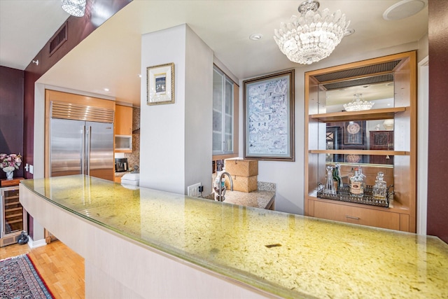 kitchen featuring light hardwood / wood-style flooring, hanging light fixtures, light stone counters, a notable chandelier, and beverage cooler