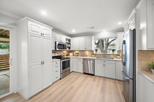 kitchen with sink, white cabinetry, crown molding, stainless steel appliances, and light hardwood / wood-style floors