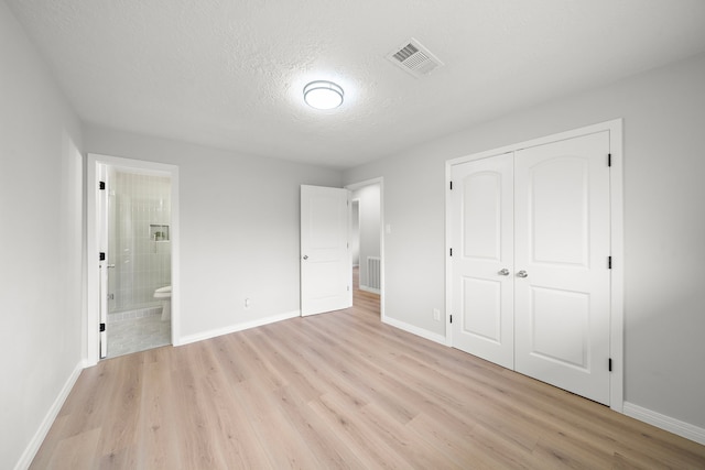 unfurnished bedroom with ensuite bathroom, light hardwood / wood-style floors, a closet, and a textured ceiling