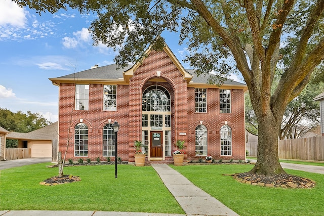 view of front facade with roof with shingles, brick siding, a front yard, fence, and driveway