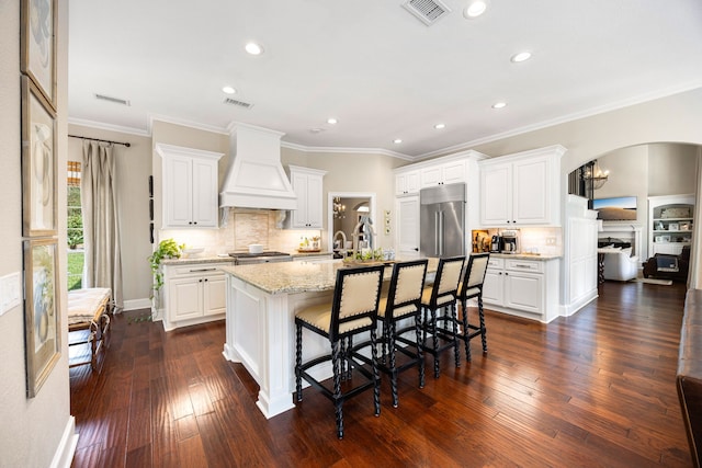 kitchen featuring appliances with stainless steel finishes, a breakfast bar area, white cabinets, custom range hood, and a center island with sink