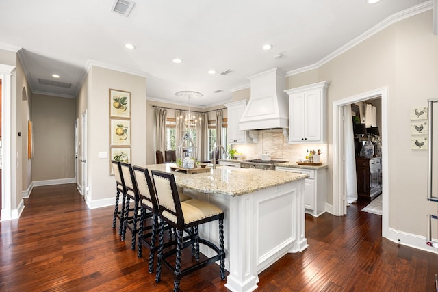 kitchen with premium range hood, white cabinetry, an island with sink, a kitchen bar, and light stone countertops