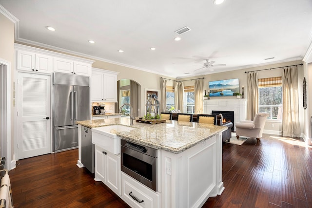 kitchen featuring built in appliances, an island with sink, and white cabinets