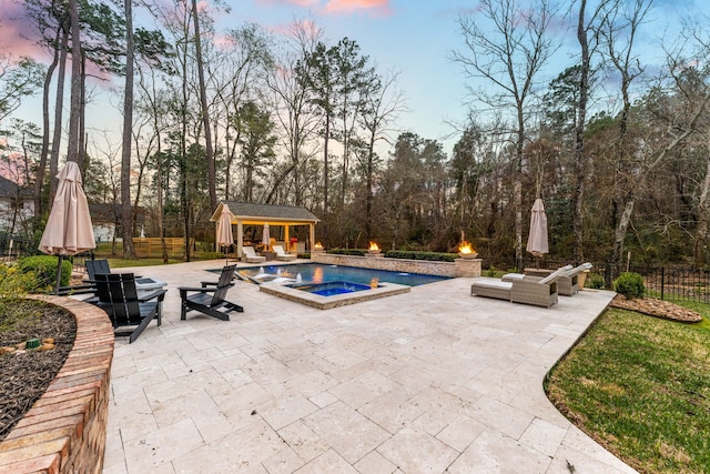 pool at dusk with an outdoor hot tub, an outbuilding, and a patio