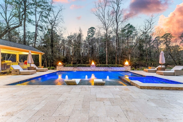 pool at dusk featuring an in ground hot tub, pool water feature, and a patio area