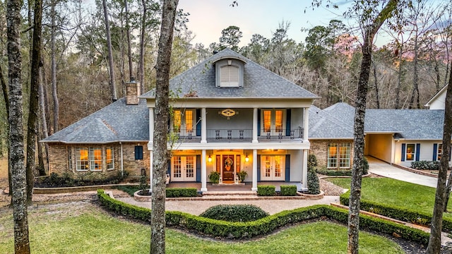 rear view of property featuring french doors, a balcony, a yard, and a porch