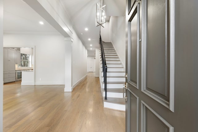 entrance foyer featuring wine cooler, ornamental molding, an inviting chandelier, and light wood-type flooring