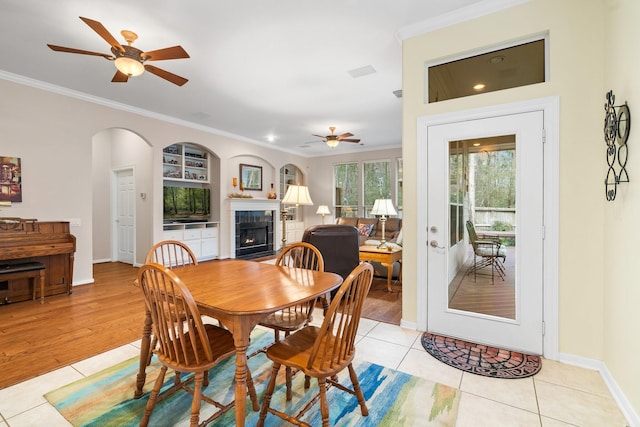 tiled dining room with ceiling fan, crown molding, a tile fireplace, and built in shelves