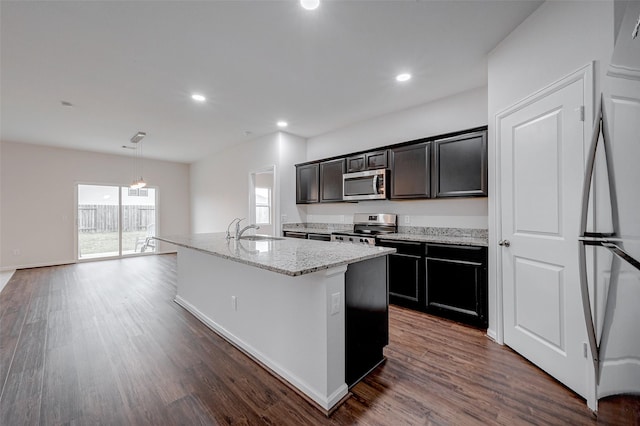 kitchen with sink, appliances with stainless steel finishes, dark hardwood / wood-style floors, light stone countertops, and a kitchen island with sink