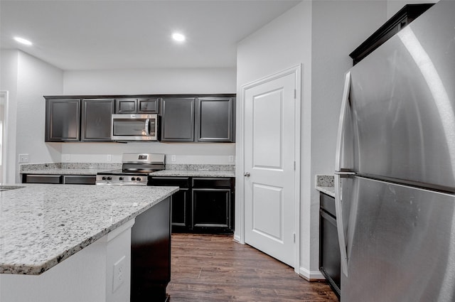 kitchen with dark wood-type flooring, appliances with stainless steel finishes, and light stone countertops