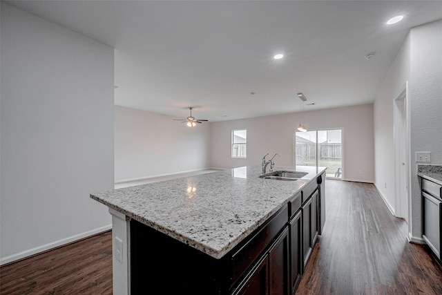 kitchen with pendant lighting, sink, dark hardwood / wood-style flooring, light stone counters, and a center island with sink