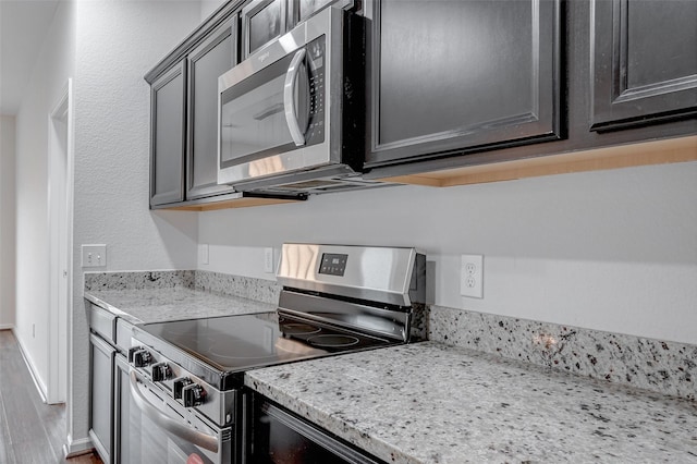 kitchen with light stone countertops, appliances with stainless steel finishes, and hardwood / wood-style floors