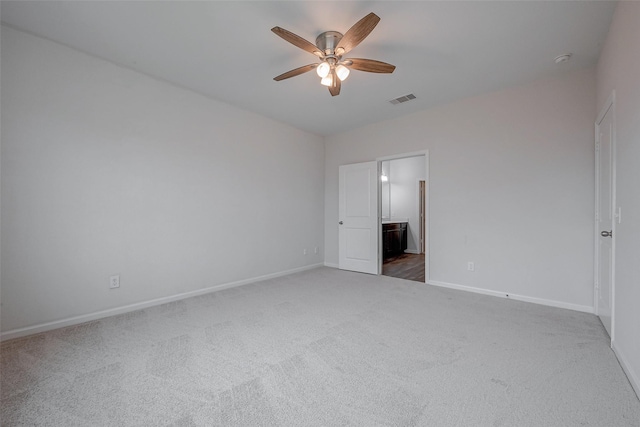 unfurnished bedroom featuring connected bathroom, dark carpet, and ceiling fan