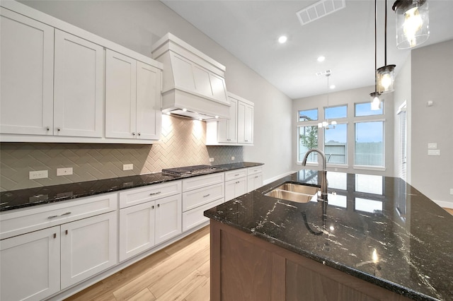 kitchen with white cabinetry, sink, hanging light fixtures, and dark stone counters