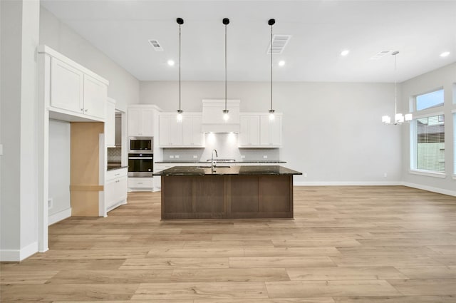 kitchen featuring hanging light fixtures, a center island with sink, white cabinets, and backsplash