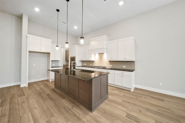 kitchen with white cabinetry, dark stone countertops, sink, and a center island with sink