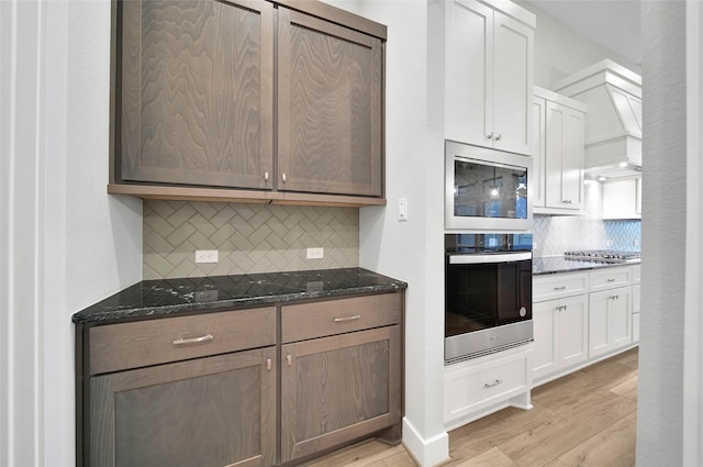 kitchen with appliances with stainless steel finishes, dark stone countertops, white cabinets, decorative backsplash, and light hardwood / wood-style floors