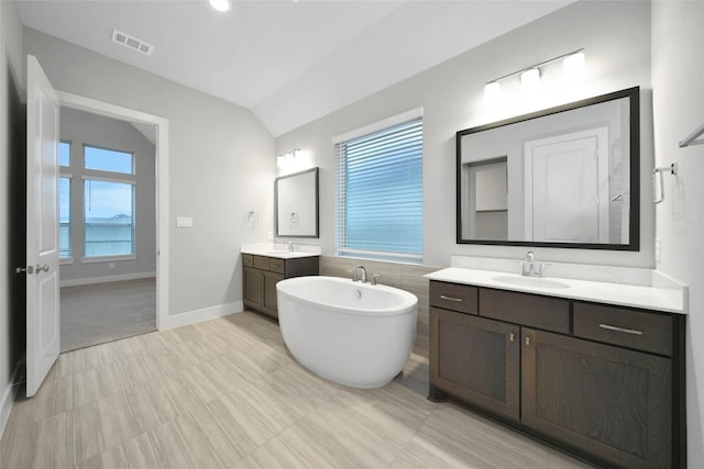 bathroom featuring vanity, lofted ceiling, a tub, and a healthy amount of sunlight