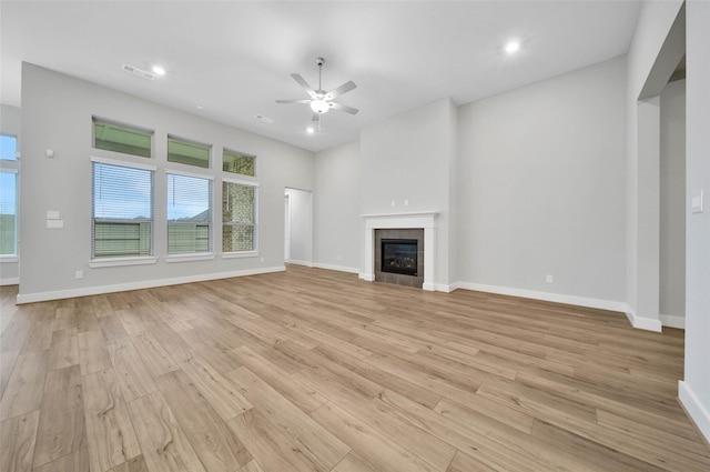 unfurnished living room with a tiled fireplace, ceiling fan, and light hardwood / wood-style floors