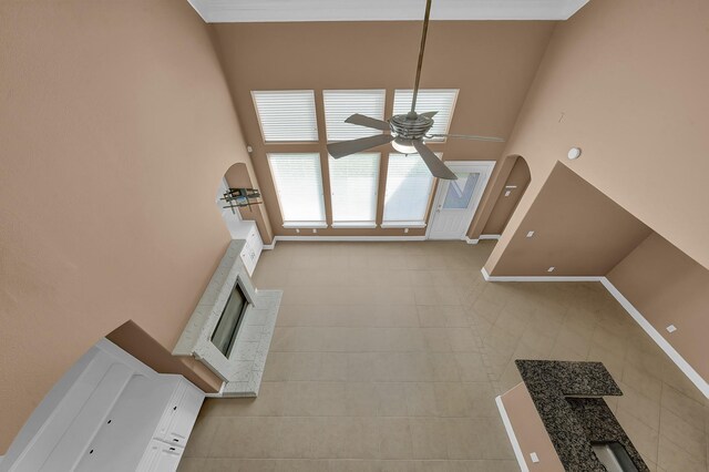 unfurnished living room with a ceiling fan, a high ceiling, a fireplace, tile patterned flooring, and baseboards