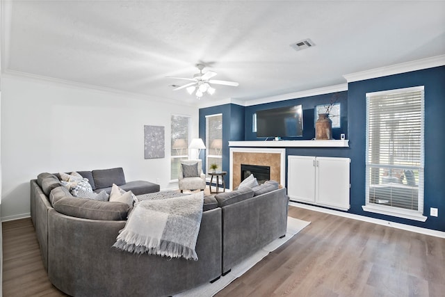 living room with a tiled fireplace, wood-type flooring, ornamental molding, and ceiling fan