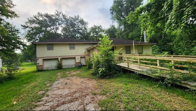 rear view of property featuring a garage, a yard, dirt driveway, and stucco siding