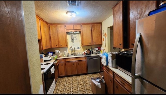 kitchen featuring brown cabinetry, stainless steel appliances, a textured ceiling, light countertops, and a sink