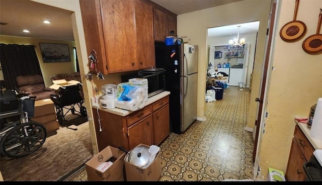 kitchen with stove, brown cabinets, freestanding refrigerator, an inviting chandelier, and light countertops