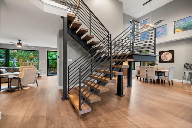 stairs featuring hardwood / wood-style floors, a towering ceiling, and ceiling fan