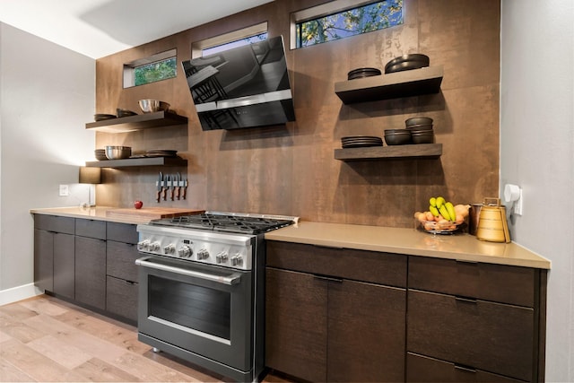 kitchen featuring decorative backsplash, wall chimney exhaust hood, dark brown cabinetry, stainless steel range with gas stovetop, and light hardwood / wood-style flooring